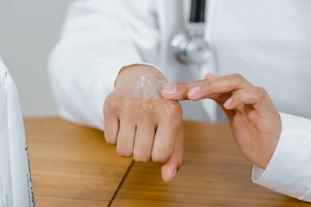 Close-up of a doctor applying lotion on their hand, focusing on skincare.